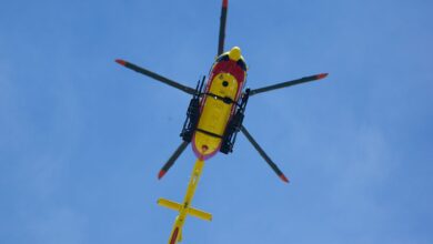 Vibrant yellow rescue helicopter soaring with rotors spinning against a clear blue sky.