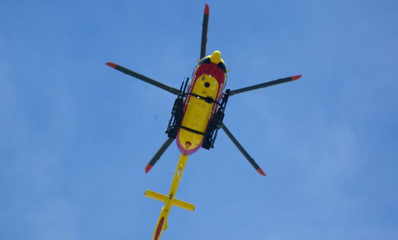 Vibrant yellow rescue helicopter soaring with rotors spinning against a clear blue sky.