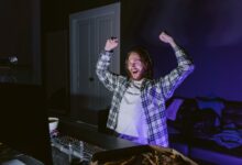 Joyful gamer celebrating victory while playing video games at night, wearing headphones.