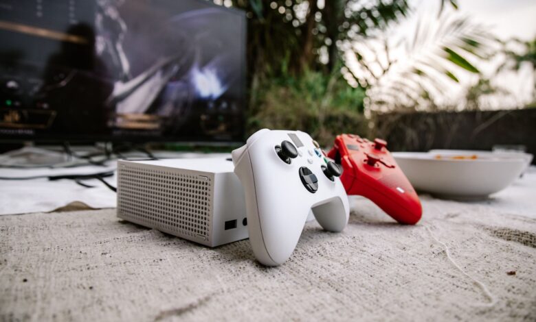 White and red game controllers on carpet with TV in the background, set outdoors.