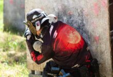 A paintball player in protective gear crouches behind cover, ready for action on the field.