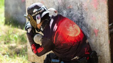 A paintball player in protective gear crouches behind cover, ready for action on the field.