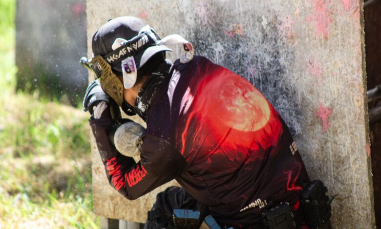 A paintball player in protective gear crouches behind cover, ready for action on the field.