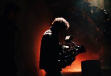 A professional cameraman captures footage in a creatively lit, moody setting, backlit by warm light.