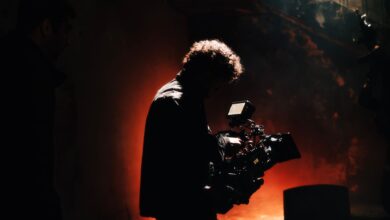 A professional cameraman captures footage in a creatively lit, moody setting, backlit by warm light.