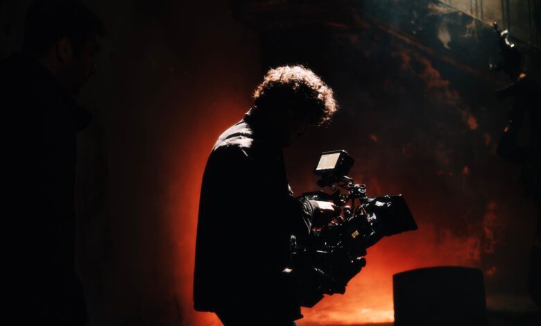 A professional cameraman captures footage in a creatively lit, moody setting, backlit by warm light.