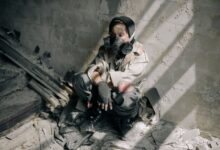 A young person in a gas mask sits in a decaying, abandoned building, evoking themes of survival and desolation.
