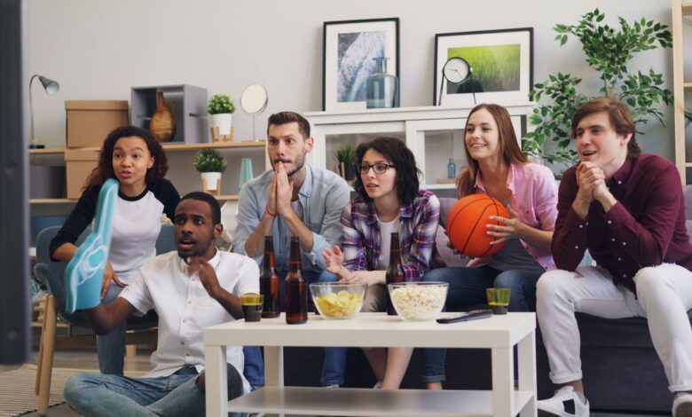 A group of young friends enthusiastically watching a sports event indoors with snacks and drinks.