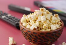 A delicious bowl of popcorn with remote and document on a pink surface, perfect for movie nights.