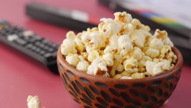A delicious bowl of popcorn with remote and document on a pink surface, perfect for movie nights.