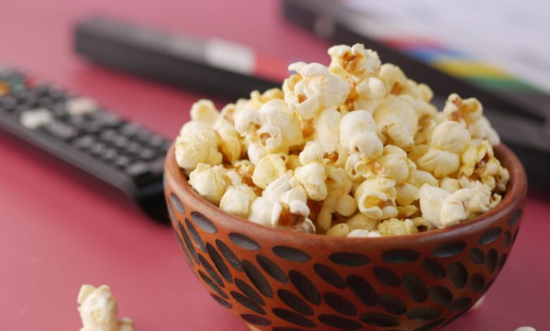 A delicious bowl of popcorn with remote and document on a pink surface, perfect for movie nights.