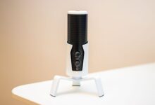 Minimalist close-up of a sleek black microphone on a modern white table, ideal for podcasts and broadcasting.