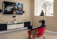 A young man wearing headphones plays video games in a modern living room setup.