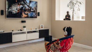 A young man wearing headphones plays video games in a modern living room setup.