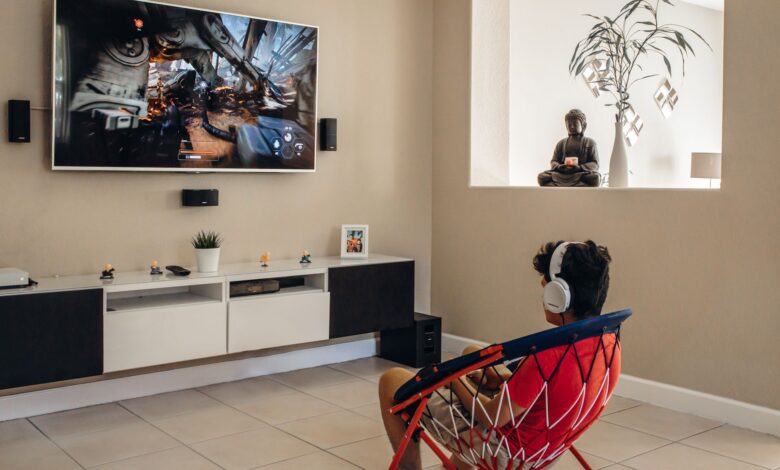 A young man wearing headphones plays video games in a modern living room setup.