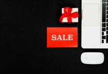 Flat lay of a laptop, gift box, and sale sign for online shopping promotion.