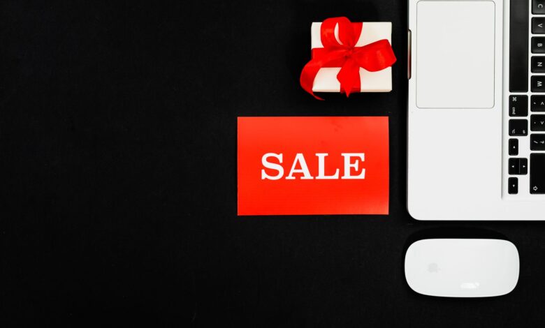 Flat lay of a laptop, gift box, and sale sign for online shopping promotion.