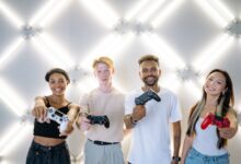 Four friends holding game controllers and smiling, enjoying time together indoors.