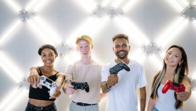 Four friends holding game controllers and smiling, enjoying time together indoors.