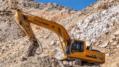 Yellow Hyundai excavator operating in a rocky quarry under a clear blue sky. Perfect for industrial themes.