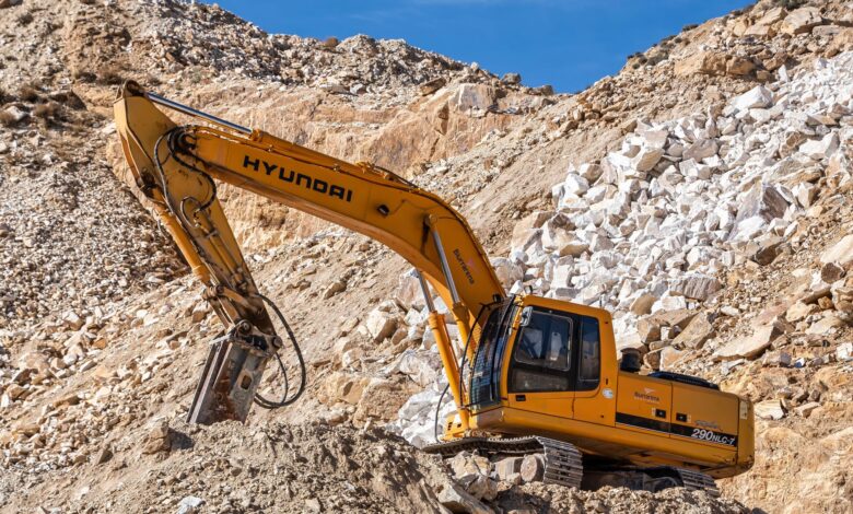 Yellow Hyundai excavator operating in a rocky quarry under a clear blue sky. Perfect for industrial themes.