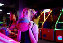 Two young women playing basketball games at a vibrant arcade, enjoying a fun night out.
