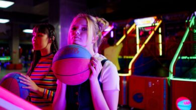 Two young women playing basketball games at a vibrant arcade, enjoying a fun night out.