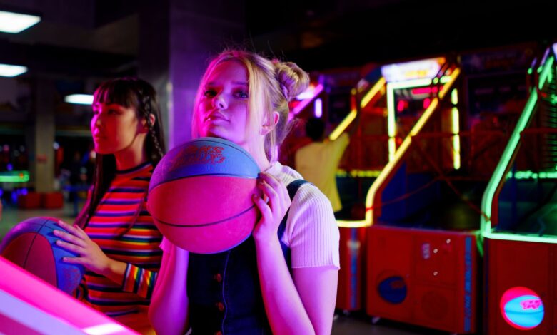 Two young women playing basketball games at a vibrant arcade, enjoying a fun night out.