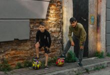 Two boys playing with soccer balls on a rustic urban street, enjoying outdoor fun.