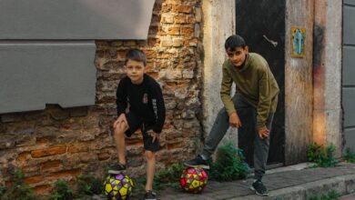 Two boys playing with soccer balls on a rustic urban street, enjoying outdoor fun.