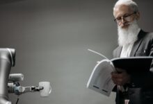 Elderly man reads as a robotic arm holds a coffee cup, showcasing technology integration.