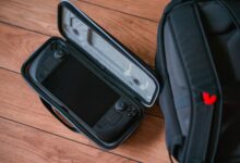 A close-up shot of a gaming console in its case next to a backpack on a wooden floor.