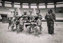 Group of soldiers in tactical gear posing in an arena for a military drill.