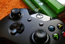 Xbox controller close-up with game cases on orange background.