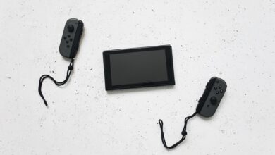 Flat lay of a Nintendo Switch and controllers on a white speckled surface, showcasing modern gaming tech.