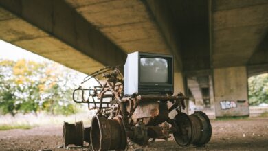 Old damaged vehicle with vintage television set on rough pathway under bridge in sunlight