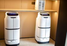Two white robotic delivery systems located in a modern indoor room with soft lighting.
