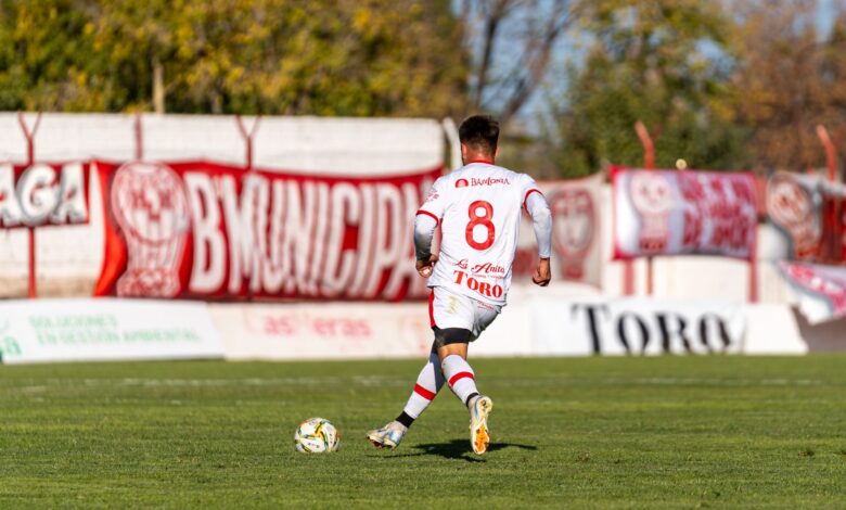 A soccer player in a white uniform dribbles the ball during a sunny outdoor match.