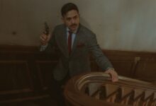 Moody scene of a man in a suit with a revolver on an ornate staircase.