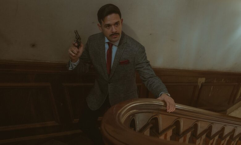 Moody scene of a man in a suit with a revolver on an ornate staircase.