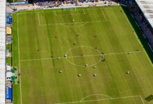 Aerial view of a football match in a sunlit stadium in Manchester.
