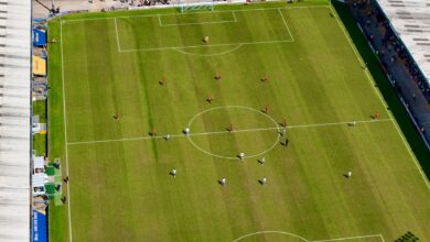 Aerial view of a football match in a sunlit stadium in Manchester.