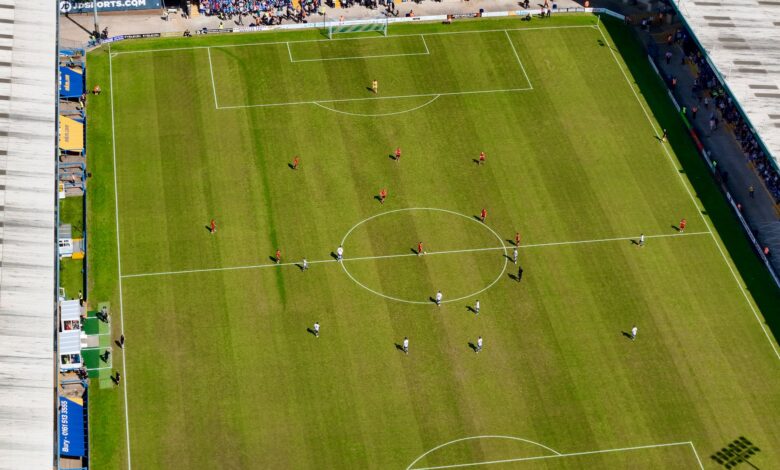 Aerial view of a football match in a sunlit stadium in Manchester.