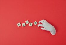 A white hand and Scrabble tiles spelling 'SCARY' on a red background, perfect for Halloween themes.