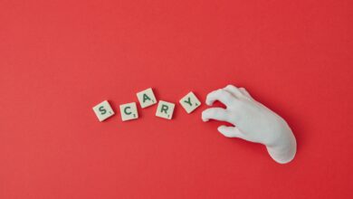 A white hand and Scrabble tiles spelling 'SCARY' on a red background, perfect for Halloween themes.