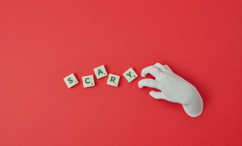 A white hand and Scrabble tiles spelling 'SCARY' on a red background, perfect for Halloween themes.