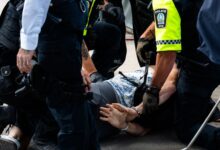 Multiple police officers detain a person on a city street, using handcuffs to restrain them.