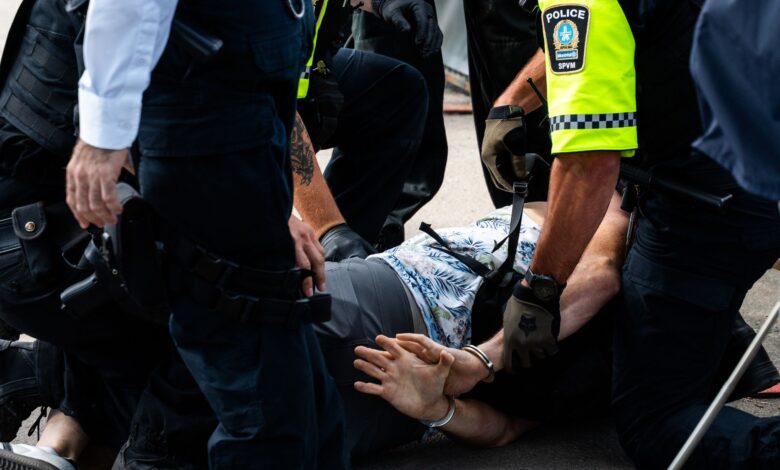 Multiple police officers detain a person on a city street, using handcuffs to restrain them.