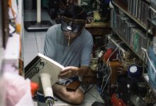A Vietnamese technician works intently repairing a vintage radio in a cluttered workshop in Hanoi.
