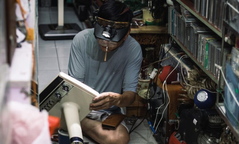 A Vietnamese technician works intently repairing a vintage radio in a cluttered workshop in Hanoi.